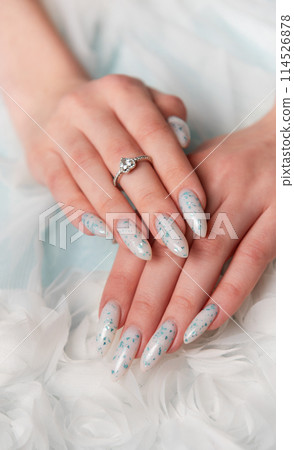 Elegant Hands Featuring Sparkling Ring and Blue Floral Manicure on Delicate White Fabric 114526878