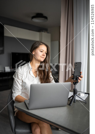 A young woman blogger conducts an educational broadcast on a laptop in social network in home workplace, online teaching concept 114526985