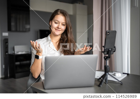 A young woman blogger conducts an educational broadcast on a laptop in social network in home workplace, online teaching concept 114526989