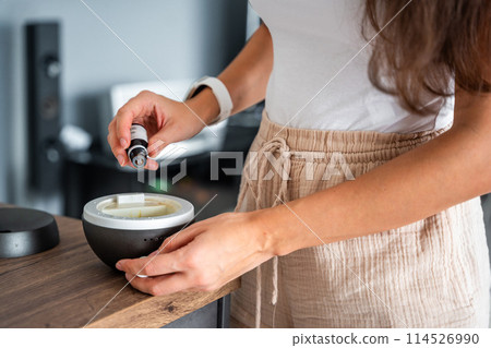 Woman adding oil to the grey aroma oil diffuser on light table at home, air freshener 114526990