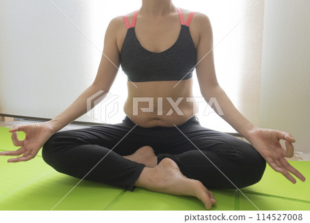 肚子上有產後妊娠紋的女士，盤腿坐在瑜珈墊上，雙手合十擺出瑜珈姿勢。 114527008