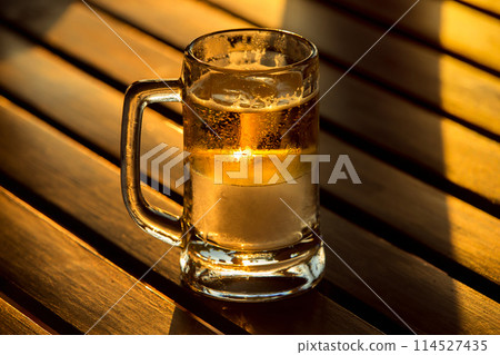 A glass of golden beer with iceat sunny sunset light at wooden table background. 114527435