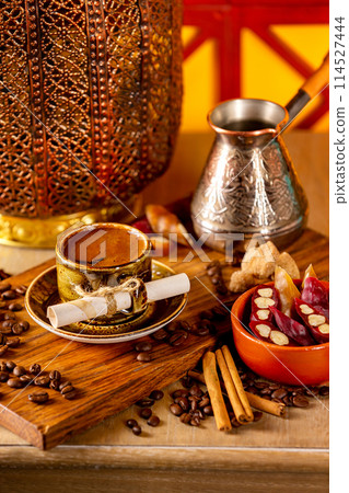 Cup of turkish black coffee on a plate at a wooden board at decorated table with candles, beans and sweets background. 114527444