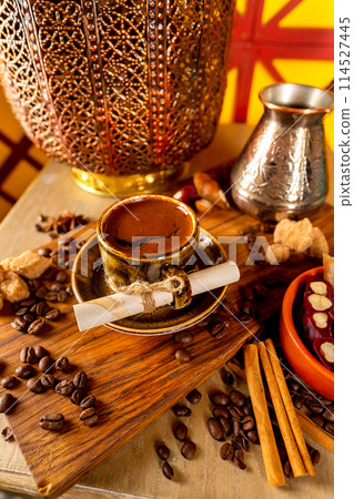 Cup of turkish black coffee on a plate at a wooden board at decorated table with candles, beans and sweets background. 114527445