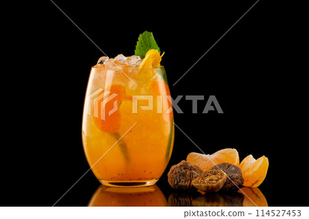 Closeup glass of orange tangerine fresh juice with ice cubes and a group of mandarin slices and figs isolated at black background. Closeup glass of orange tangerine fresh juice with ice cubes and a group of mandarin slices and figs isolated at black background. 114527453