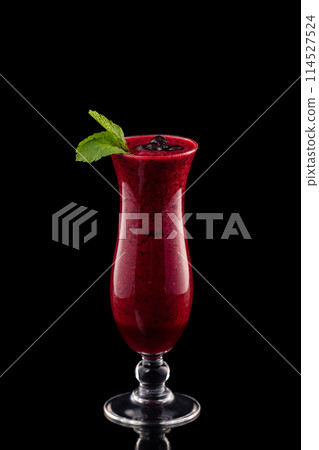 Glass of red cherry fresh shake decorated with black currant and mint isolated at black background. Glass of red cherry fresh shake decorated with black currant and mint isolated at black background. 114527524