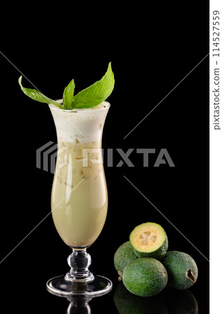 Glass of fresh pineapple guava smootjie decorated with basil isolated at black background. 114527559