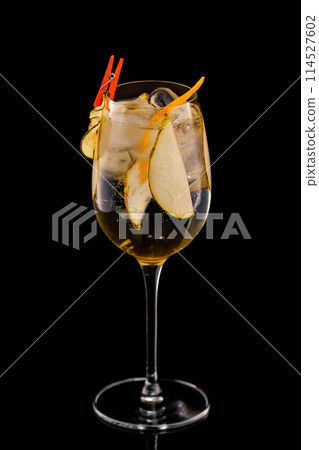 Glass of fizz cocktail with white sparkling wine and pear decorated with lemon chips isolated at black background. 114527602