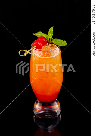 Closeup glass of fresh orange tequila sunrise cocktail decorated with mint and cherry isolated at black background. 114527615