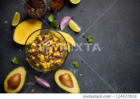 Cooking traditional tuna and mango tartare - chopped and mixed tuna, mango, cilantro and onion in a glass bowl 114527818