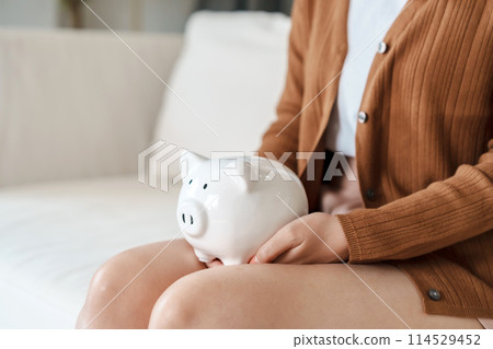 Woman hand holding piggy bank while sitting on sofa. Save money and financial investment 114529452