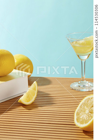 Front view at lemon theme photography on baby blue background, a white counter, cocktail glass of lemon liquid and fresh lemon decoration. Empty space for adding text or element of designing Front view at lemon theme photography on baby blue background, a white counter, cocktail glass of lemon liquid and fresh lemon decoration. Empty space for adding text or element of designing 114530306