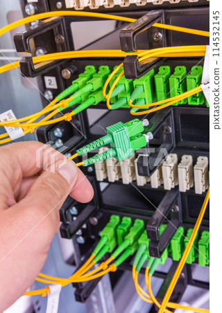 Hand of computer technician connecting fiber optics cable into data switch Hand of computer technician connecting fiber optics cable into data switch 114532145