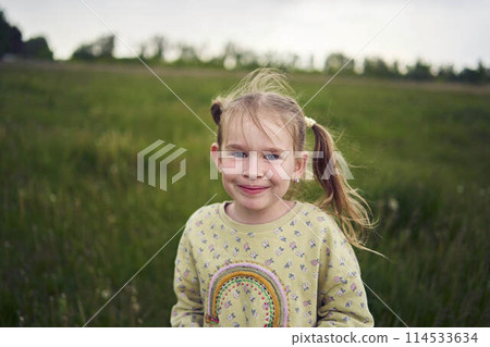 a beautiful blond girl with her toy bunny is playing in the field 114533634