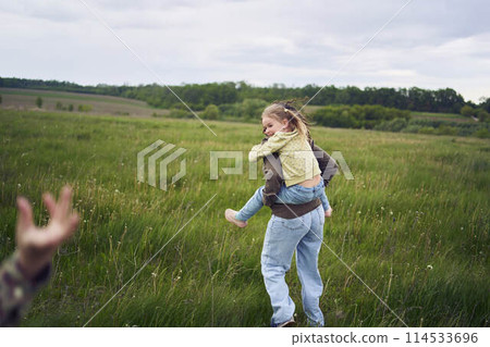 a mother rolls her daughters on her back, playing horse, kisses and hugs a mother rolls her daughters on her back, playing horse, kisses and hugs 114533696