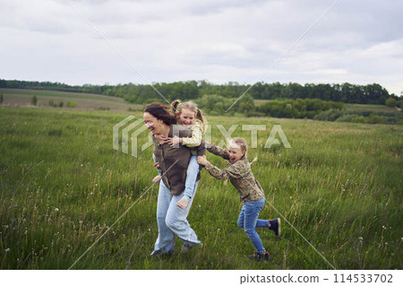 a mother rolls her daughters on her back, playing horse, kisses and hugs a mother rolls her daughters on her back, playing horse, kisses and hugs 114533702