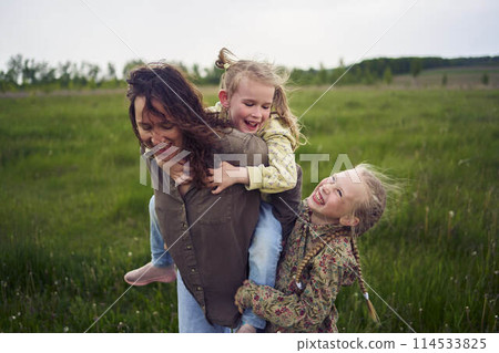 a mother rolls her daughters on her back, playing horse, kisses and hugs 114533825