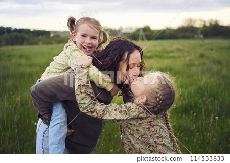 a mother rolls her daughters on her back, playing horse, kisses and hugs 114533833