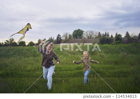 two little sisters and mother run and launch a kite in a field 114534013