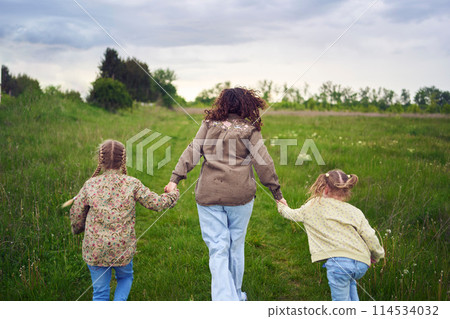 mother and children run holding hands in the field 114534032