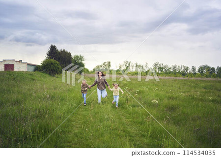 mother and children run holding hands in the field 114534035