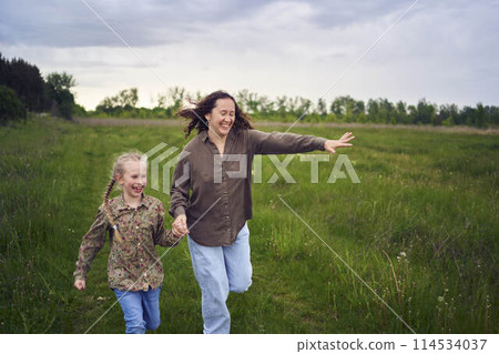 mother and children run holding hands in the field 114534037