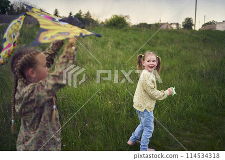 two little sisters repair and fly a kite in a field 114534318
