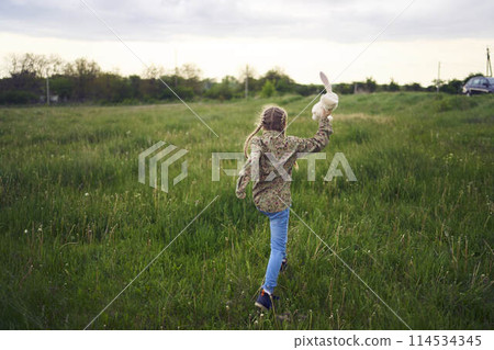 a beautiful blond girl with her toy bunny is playing in the field a beautiful blond girl with her toy bunny is playing in the field 114534345