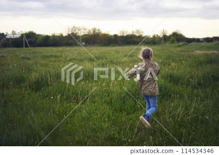 a beautiful blond girl with her toy bunny is playing in the field 114534346