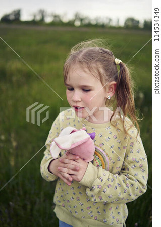a beautiful blond girl with her toy bunny is playing in the field a beautiful blond girl with her toy bunny is playing in the field 114534349