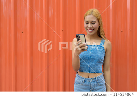 Portrait of beautiful Asian girl with blonde hair against orange background 114534864