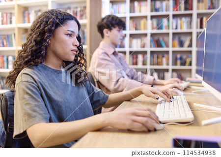 Side view portrait of Latin American teenage girl using computer in school library and doing research online Side view portrait of Latin American teenage girl using computer in school library and doing research online 114534938