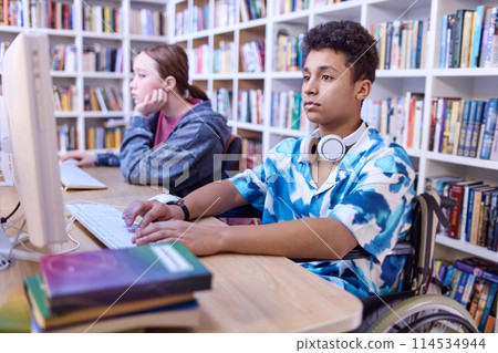 Portrait of teen boy using wheelchair in computer class at school library and doing research for project Portrait of teen boy using wheelchair in computer class at school library and doing research for project 114534944