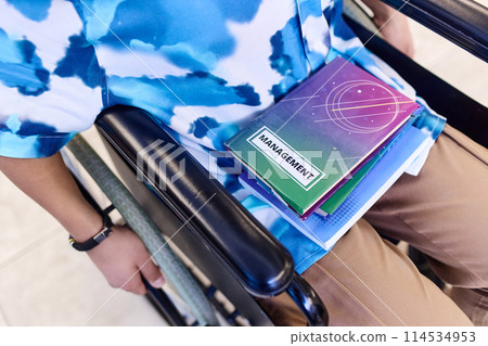 Top view closeup of teenage boy using wheelchair in school with books in lap copy space Top view closeup of teenage boy using wheelchair in school with books in lap copy space 114534953