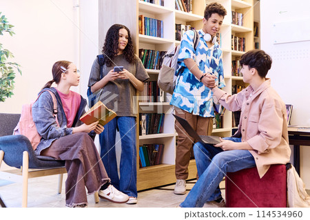 Full length portrait of multiethnic group of teenagers relaxing and chatting during break in modern school library Full length portrait of multiethnic group of teenagers relaxing and chatting during break in modern school library 114534960