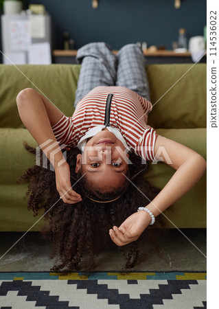 Vertical portrait of little African American girl lying upside down on sofa and looking at camera while having fun at home Vertical portrait of little African American girl lying upside down on sofa and looking at camera while having fun at home 114536022