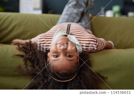 Portrait of young Black girl lying upside down on sofa at home and looking at camera copy space Portrait of young Black girl lying upside down on sofa at home and looking at camera copy space 114536031