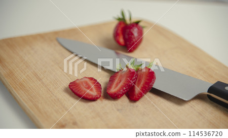 The strawberries are cut into slices. they lie on a wooden board and next to the knife 114536720