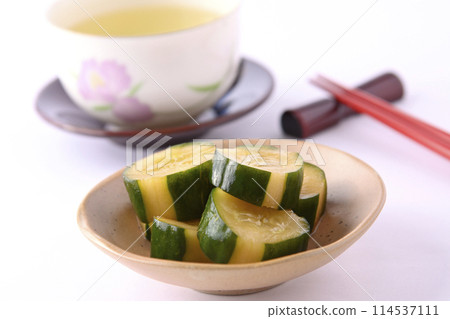 Pickled cucumbers on a small plate and chopsticks and chopstick rests in a teacup on a white background Pickled cucumbers on a small plate and chopsticks and chopstick rests in a teacup on a white background 114537111