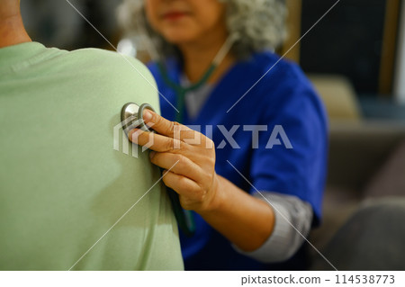 Health visitor listening to patient lungs with stethoscope during home care visit 114538773