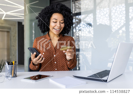 Smiling woman using smartphone for online payment with credit card in a modern office setting. Concept of e-commerce, online shopping, and technology. Smiling woman using smartphone for online payment with credit card in a modern office setting. Concept of e-commerce, online shopping, and technology. 114538827