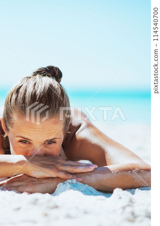Young woman in swimsuit laying on sandy beach 114540700