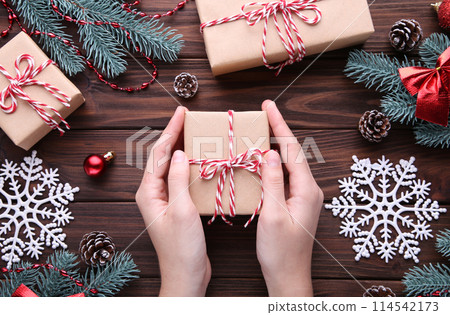 Female hands holding gift box on brown wooden table Female hands holding gift box on brown wooden table 114542173