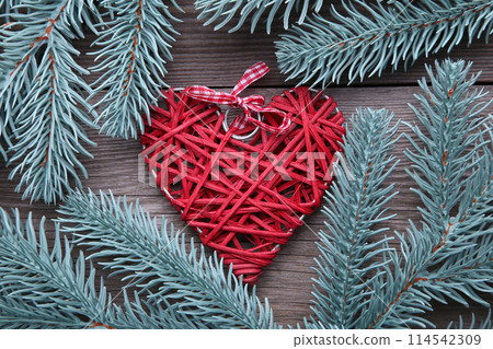 Fir tree branch with a red heart on a grey background. 114542309
