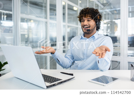 Smiling man with curly hair and wearing a headset, engaged in a video call on his laptop in a modern office environment Smiling man with curly hair and wearing a headset, engaged in a video call on his laptop in a modern office environment 114542700