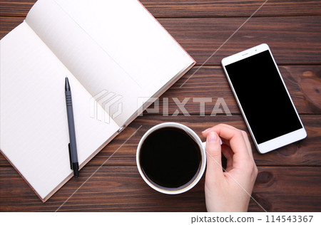 Female hands holding cup of coffee and smartphone on brown wooden background. 114543367