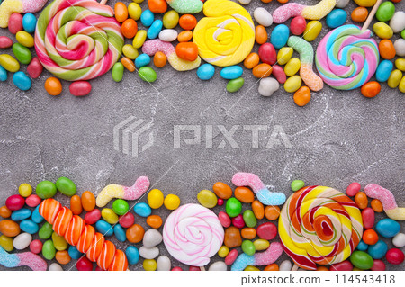 Colorful lollipop and different colored round candy on grey concrete background Colorful lollipop and different colored round candy on grey concrete background 114543418