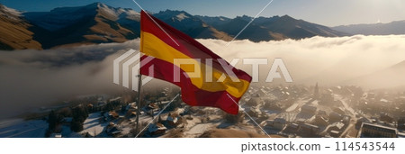 bold Spanish flag dances in the wind against a clear blue sky, casting a patriotic light over the picturesque town below. 114543544
