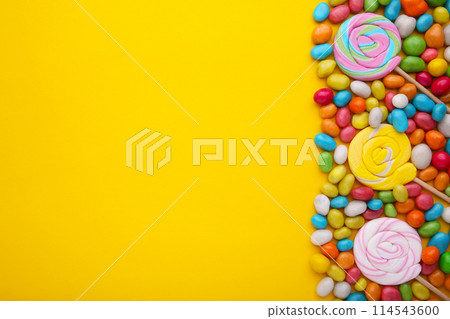 Colorful lollipops and different colored round candy on yellow background 114543600