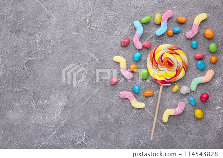 Colorful lollipop and different colored round candy on grey background Colorful lollipop and different colored round candy on grey background 114543828